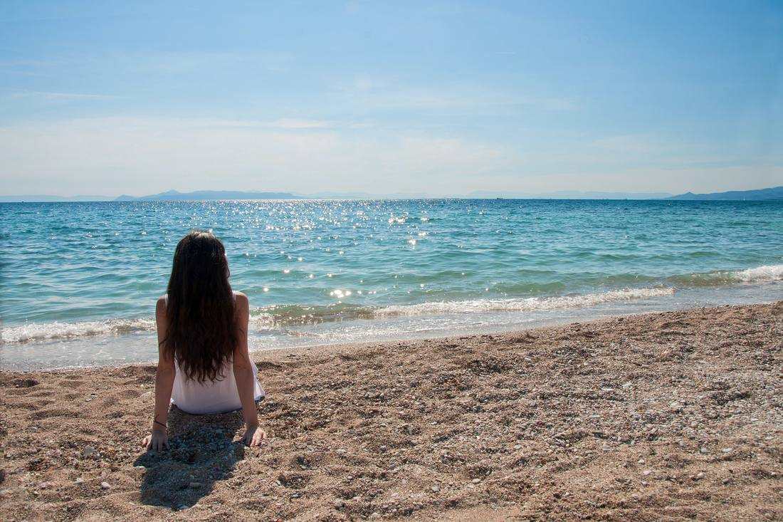 A man sitting on the sand, looking out at the ocean