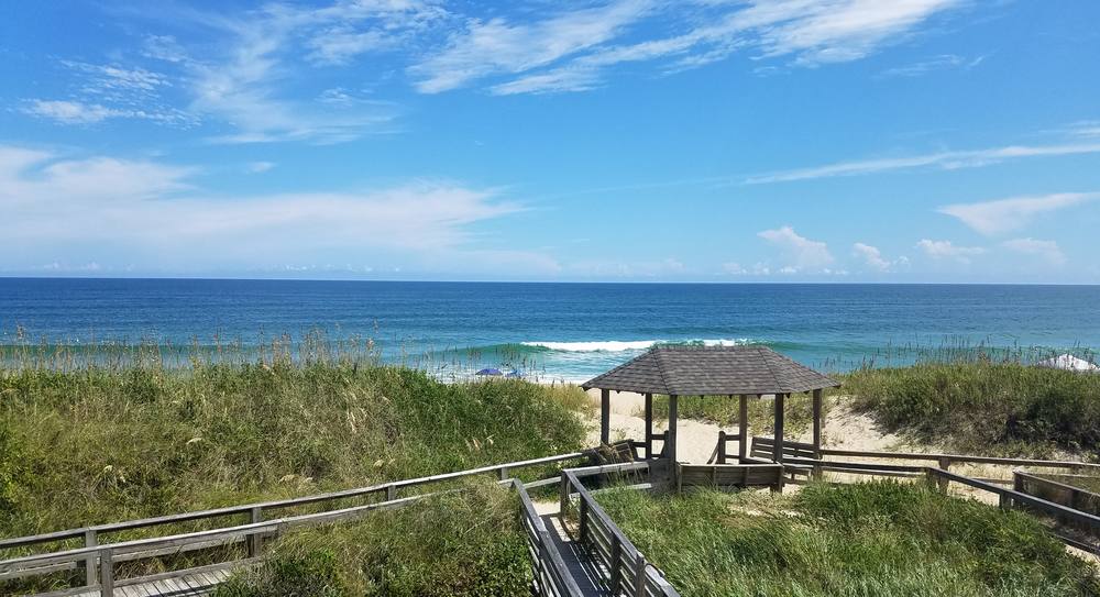 A wooden boardwalk winding through dune grass down to the ocean